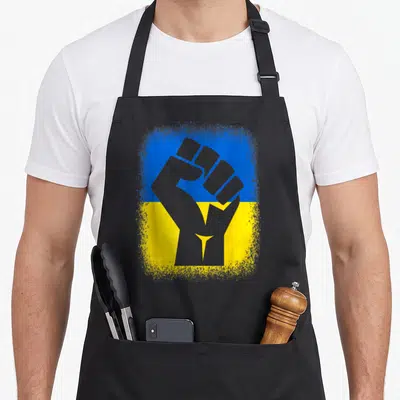 Stand ukrainian aprons - Grey raised fist silhouette over distressed blue and yellow flag background — shown on a black cotton canvas apron against a white background