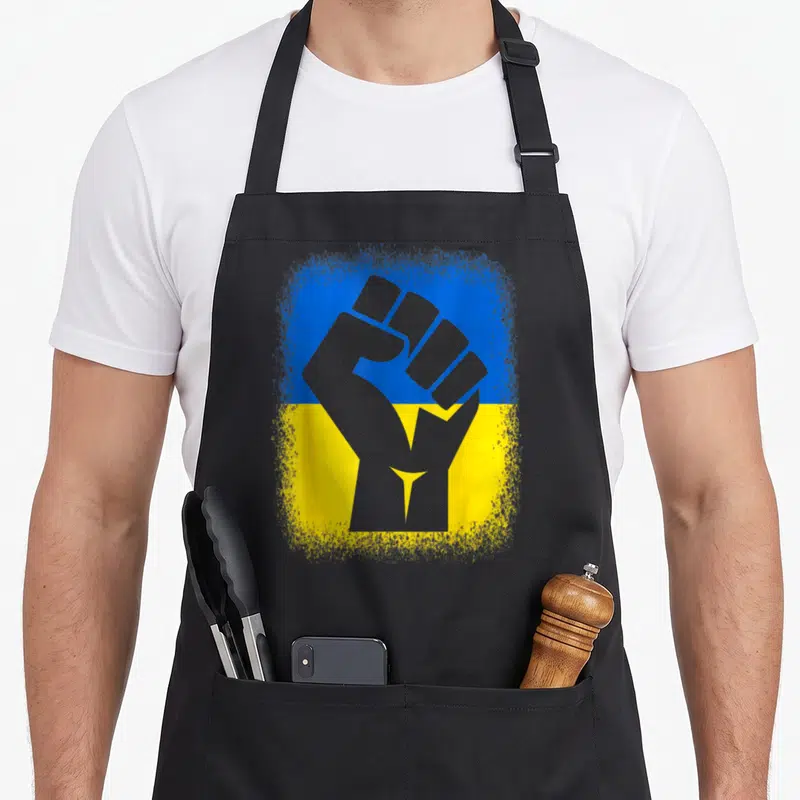 Stand ukrainian aprons - Grey raised fist silhouette over distressed blue and yellow flag background — shown on a black cotton canvas apron against a white background