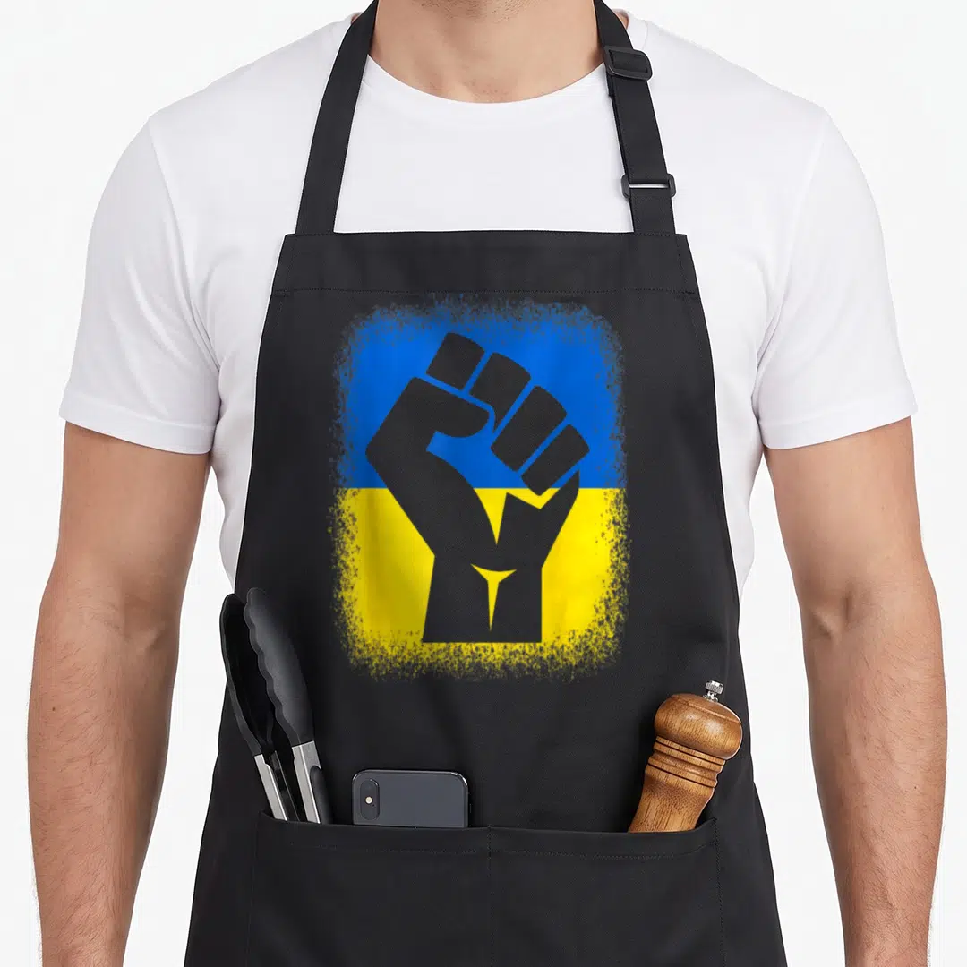 Stand ukrainian aprons - Grey raised fist silhouette over distressed blue and yellow flag background — shown on a black cotton canvas apron against a white background