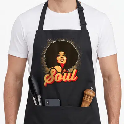 Afro soul 70s apron - Cartoon woman with large afro and Soul script in orange and red dots — shown on a black cotton canvas apron against a white background