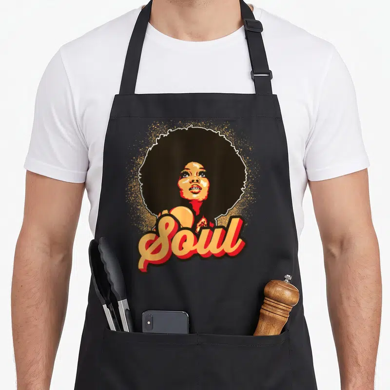 Afro soul 70s apron - Cartoon woman with large afro and Soul script in orange and red dots — shown on a black cotton canvas apron against a white background