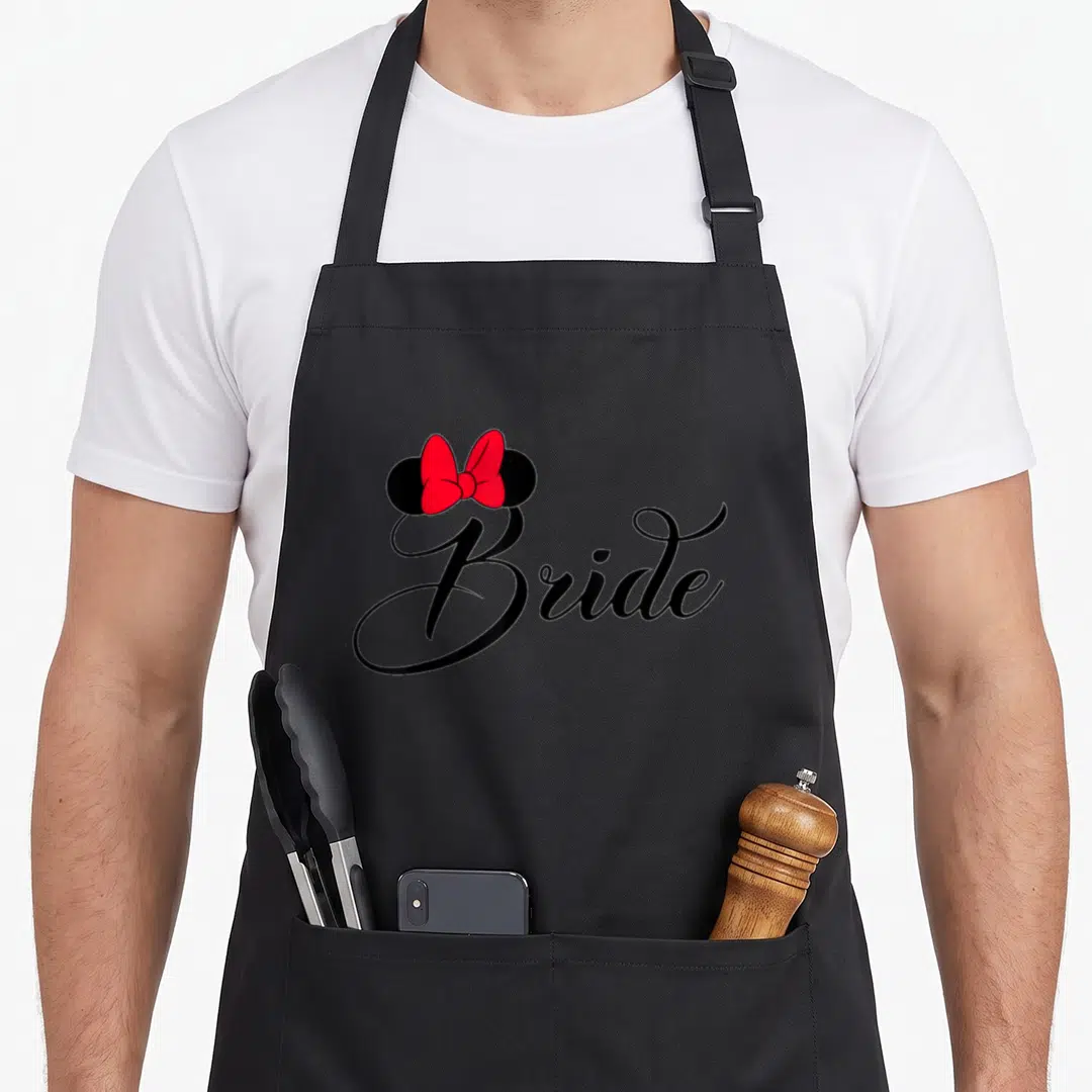 Bow bridal apron - Black Bride script with red bow and black ear circles — shown on a black cotton canvas apron against a white background