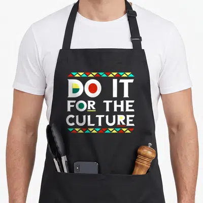 Culture african print apron - Stacked white text DO IT FOR THE CULTURE with red yellow teal green triangle borders — shown on a black cotton canvas apron against a white background