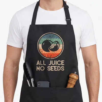 Vasectomy funny juice apron - Retro citrus emblem over striped background with ALL JUICE NO SEEDS text — shown on a black cotton canvas apron against a white background
