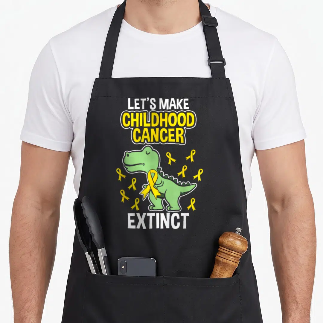 Childhood dinosaur apron - Green cartoon dinosaur holding yellow ribbon with Let's Make Childhood Cancer Extinct text — shown on a black cotton canvas apron against a white background