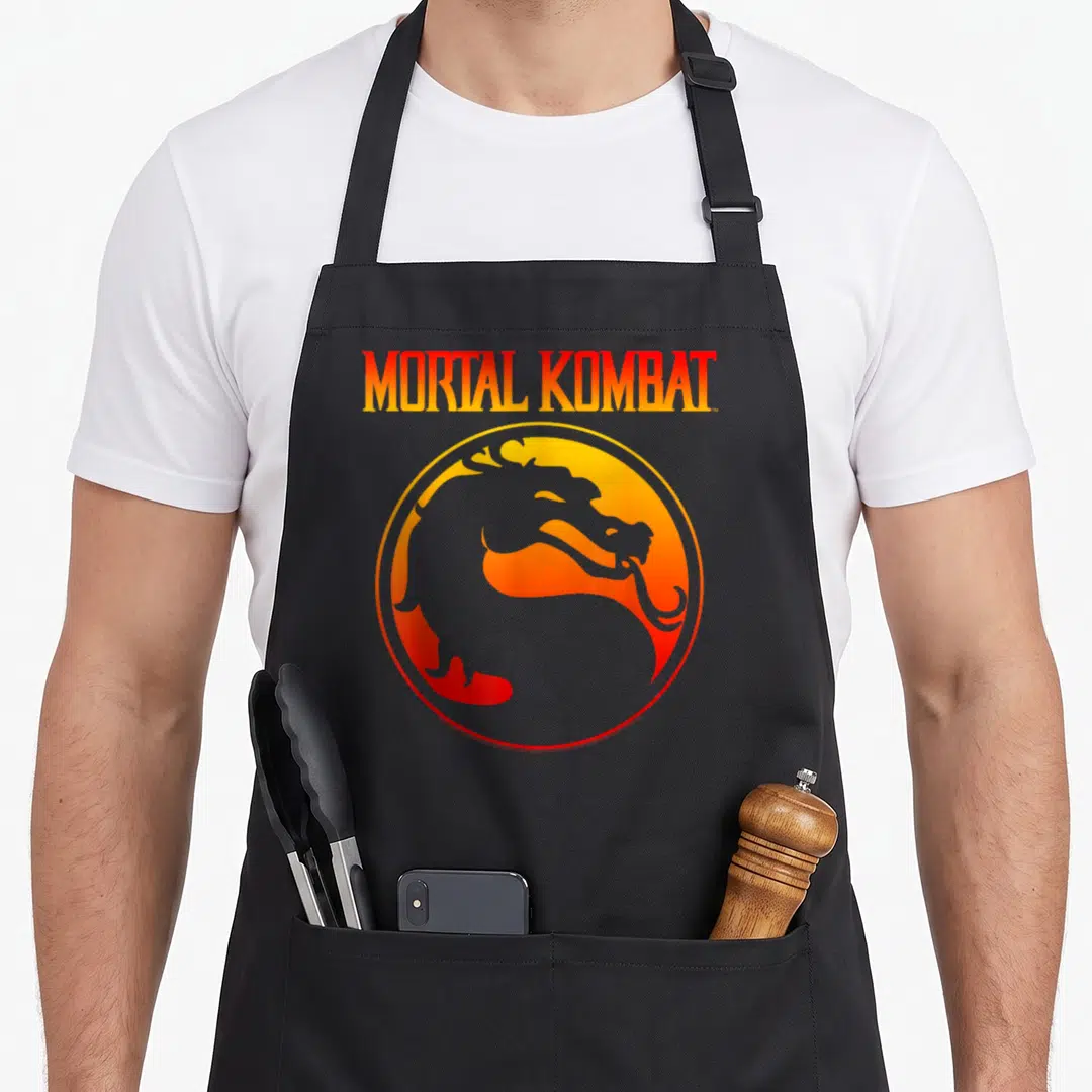 Klassic video game apron - MORTAL KOMBAT gradient text above circular orange yellow grey dragon silhouette emblem — shown on a black cotton canvas apron against a white background