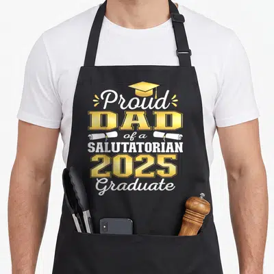 Proud graduate salutatorian apron - Proud DAD 2025 Salutatorian text with cap and two diplomas — shown on a black cotton canvas apron against a white background
