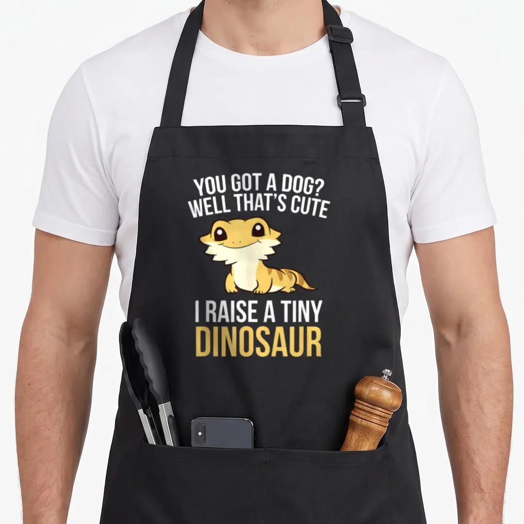 Dragon tiny chef apron - Cartoon bearded dragon between YOU GOT A DOG text in white and yellow — shown on a black cotton canvas apron against a white background