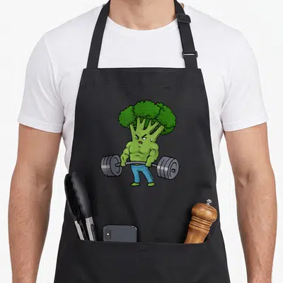 Deadlift bodybuilding apron - Cartoon muscular broccoli lifting grey barbell wearing blue pants — shown on a black cotton canvas apron against a white background