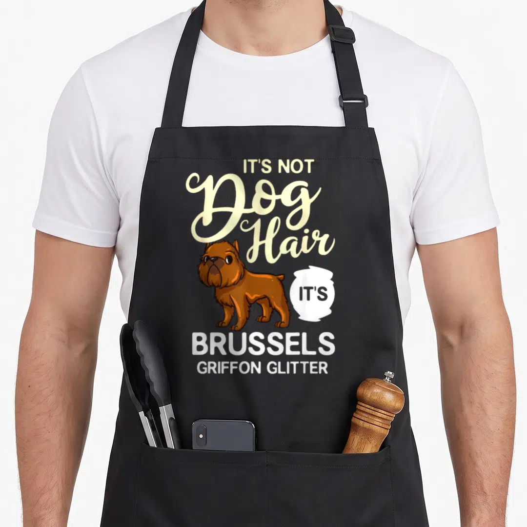 Griffon puppy dog apron - Cartoon brown Brussels Griffon dog with It's Not Dog Hair Brussels Griffon Glitter text — shown on a black cotton canvas apron against a white background