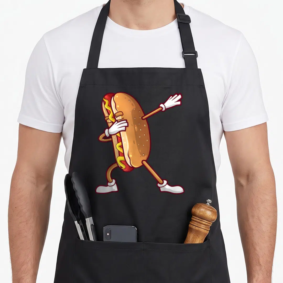 Dabbing hot dog apron - Cartoon hot dog with white gloves and shoes dancing in tan, red, and yellow — shown on a black cotton canvas apron against a white background