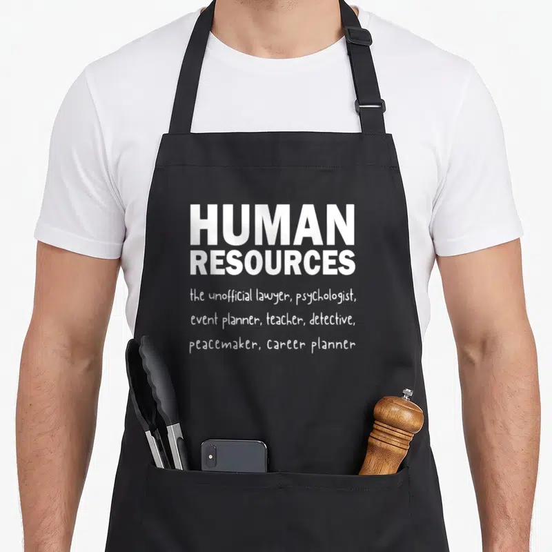 Definition hr apron - White text reading HUMAN RESOURCES the unofficial lawyer psychologist event planner teacher — shown on a black cotton canvas apron against a white background