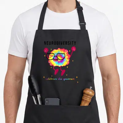 Autistic autism acceptance apron - Tie-dye brain with glasses and raised fists surrounded by stars and neurodiversity — shown on a black cotton canvas apron against a white background