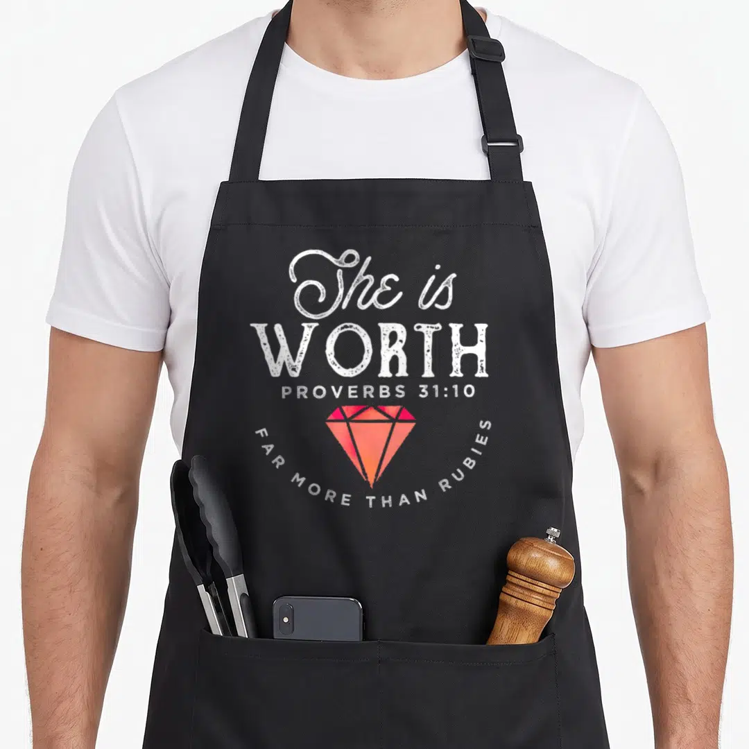 She the ruby apron - White stacked text and red orange diamond graphic on black bib apron — shown on a black cotton canvas apron against a white background