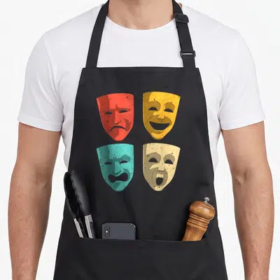 Theatre mask theater apron - Four distressed drama masks in red, yellow, teal, and beige arranged in a grid pattern — shown on a black cotton canvas apron against a white background