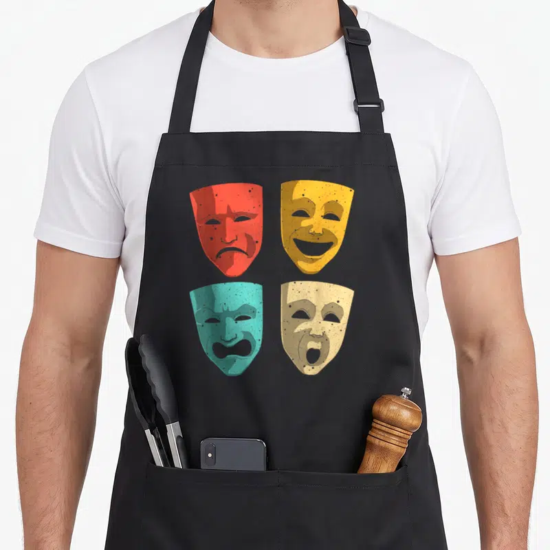 Theatre mask theater apron - Four distressed drama masks in red, yellow, teal, and beige arranged in a grid pattern — shown on a black cotton canvas apron against a white background