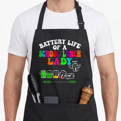 Battery lunch lady apron - Stacked rainbow text above six cartoon batteries fading from full green charge to a white — shown on a black cotton canvas apron against a white background