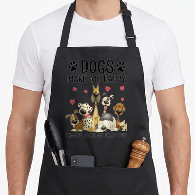Human dog apron - Six cartoon dogs with red hearts and text DOGS MAKE ME HAPPY HUMANS MAKE MY HEAD HURT — shown on a black cotton canvas apron against a white background