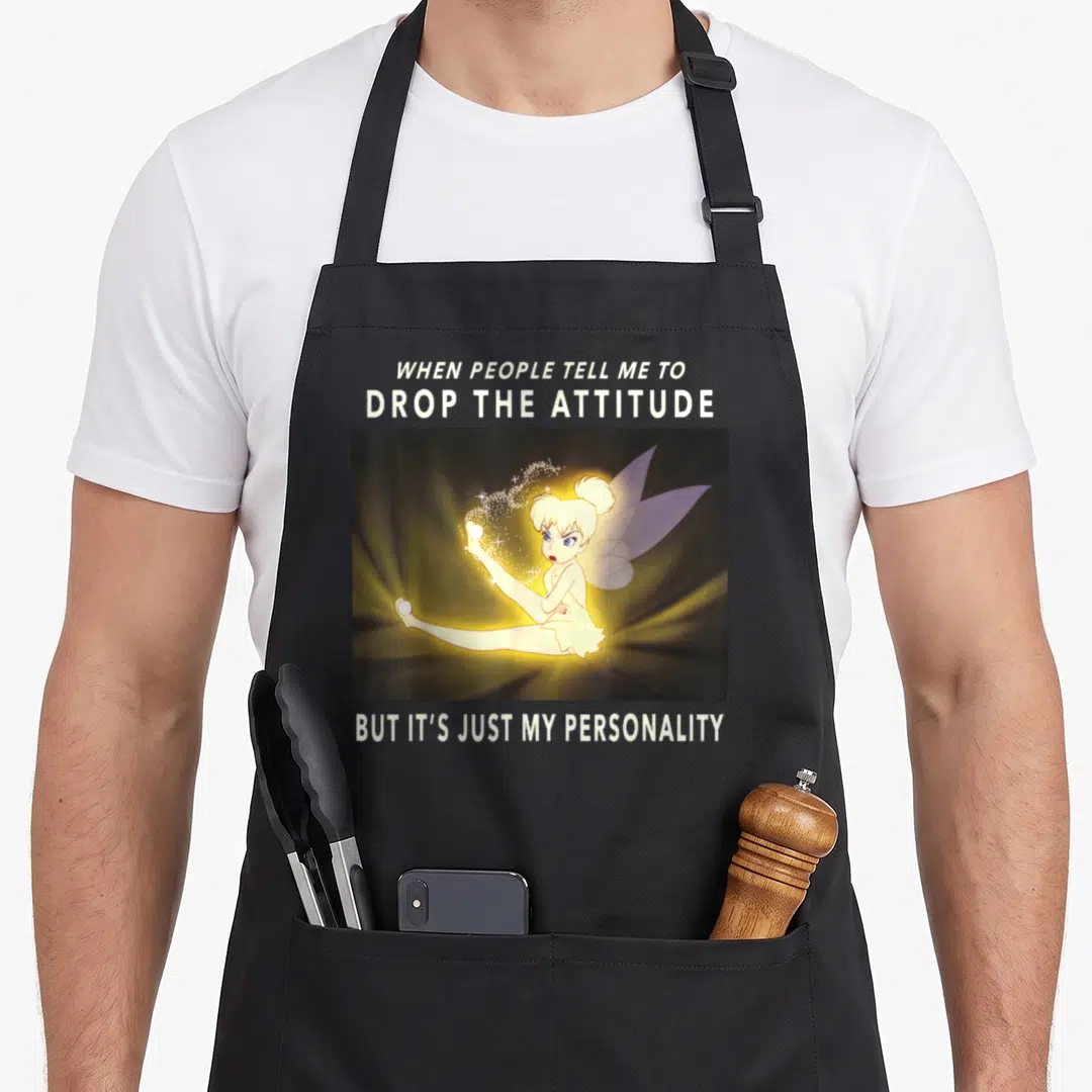 Peter meme apron - Fairy sitting with magic dust under text about dropping attitude and personality — shown on a black cotton canvas apron against a white background