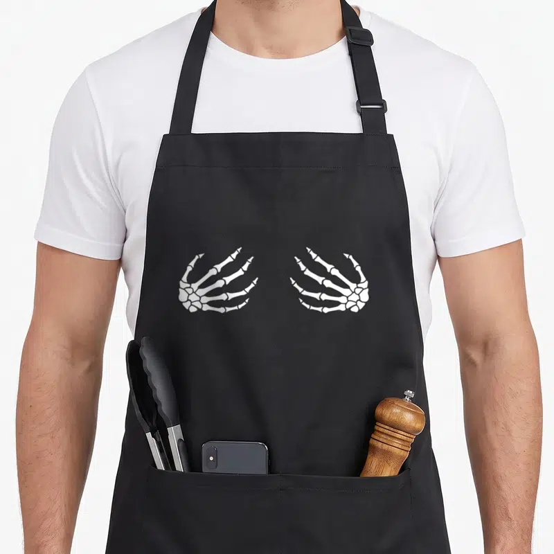 Skeleton halloween apron - Two white skeleton hands facing inward in black line art on grey background — shown on a black cotton canvas apron against a white background
