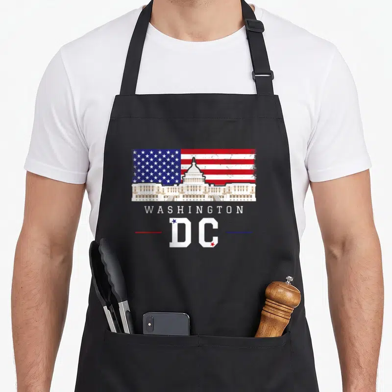 Souvenir capitol hill apron - Distressed US Capitol building over red white blue flag with WASHINGTON DC text — shown on a black cotton canvas apron against a white background