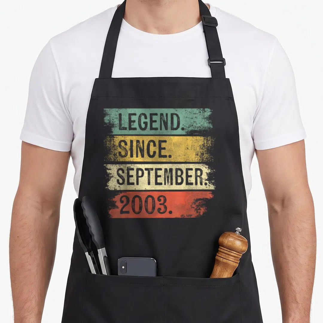 Legend september birthday apron - Stacked LEGEND SINCE SEPTEMBER 2003 text on green yellow beige and red distressed bars — shown on a black cotton canvas apron against a white background