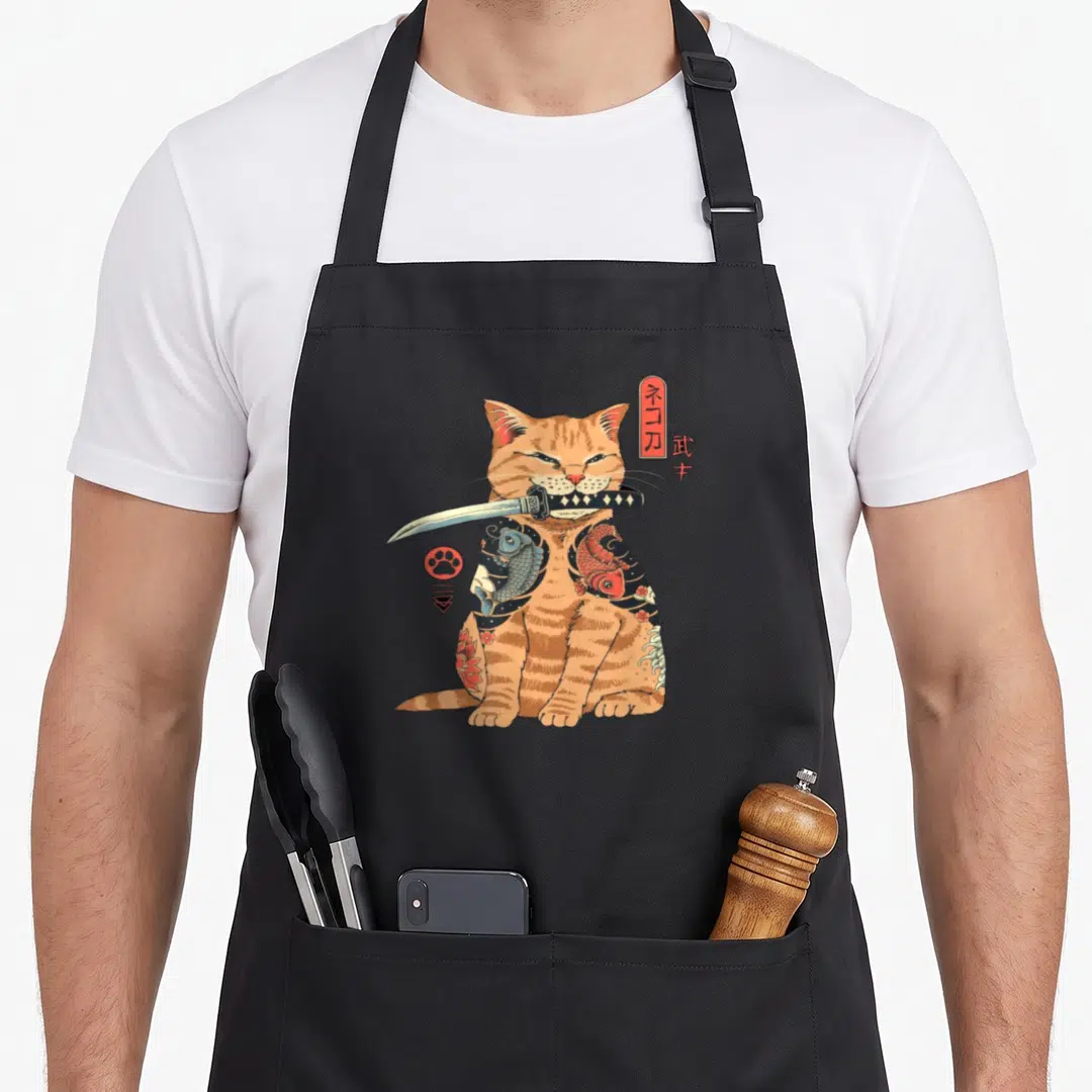 Alexamerch cat apron - Tattooed orange cat holding katana with Japanese text and paw symbol — shown on a black cotton canvas apron against a white background