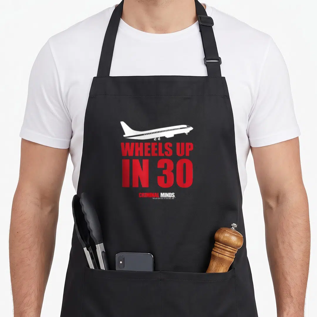 Criminal wheel apron - White airplane over red WHEELS UP IN 30 text and Criminal Minds logo on black — shown on a black cotton canvas apron against a white background