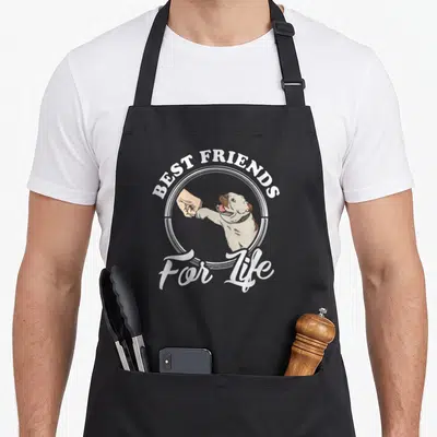 Friend english chef aprons - English Bulldog shaking human hand with text Best Friends For Life in white and brown — shown on a black cotton canvas apron against a white background