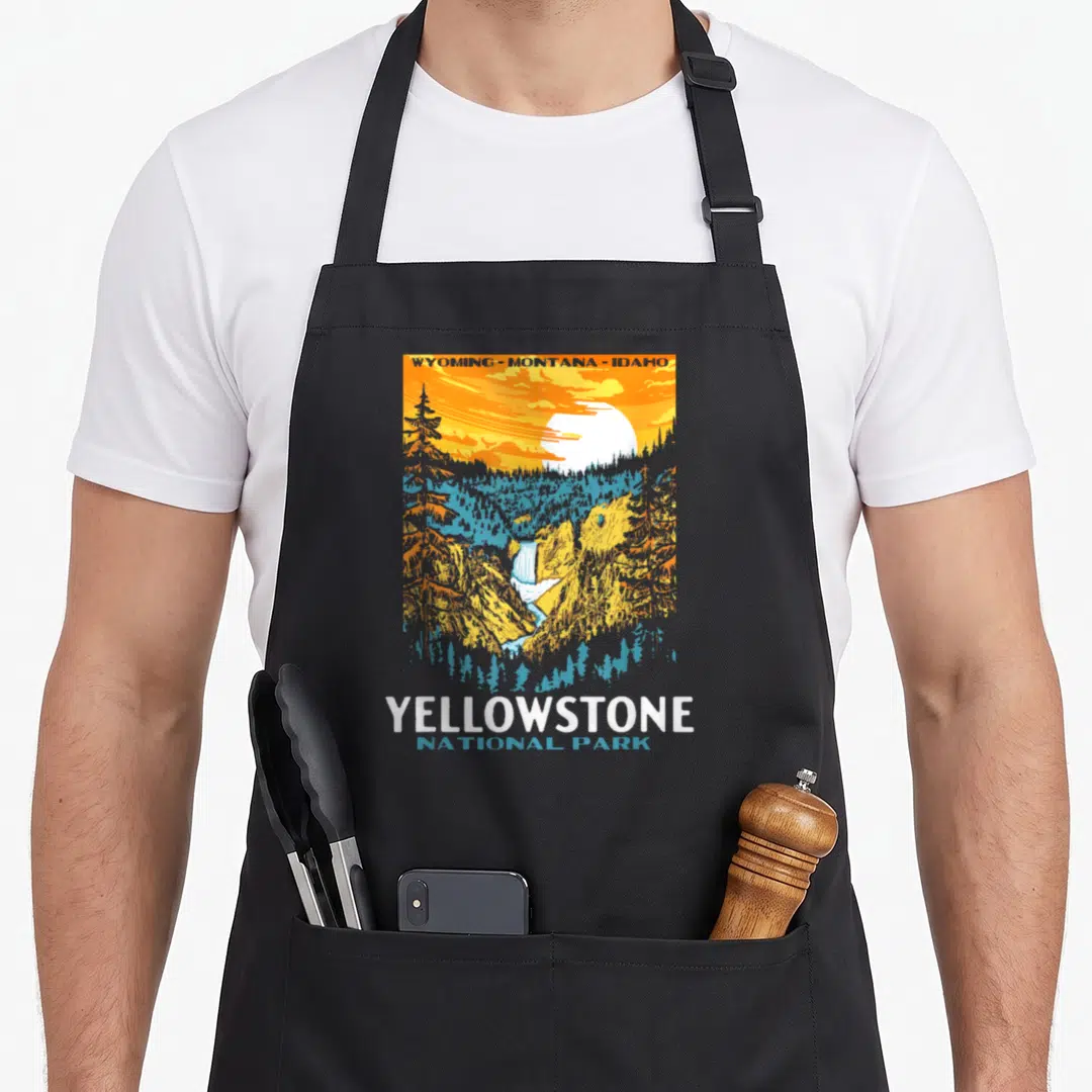 National fall apron - Retro Yellowstone landscape with WYOMING-MONTANA-IDAHO text and stacked park name in orange — shown on a black cotton canvas apron against a white background