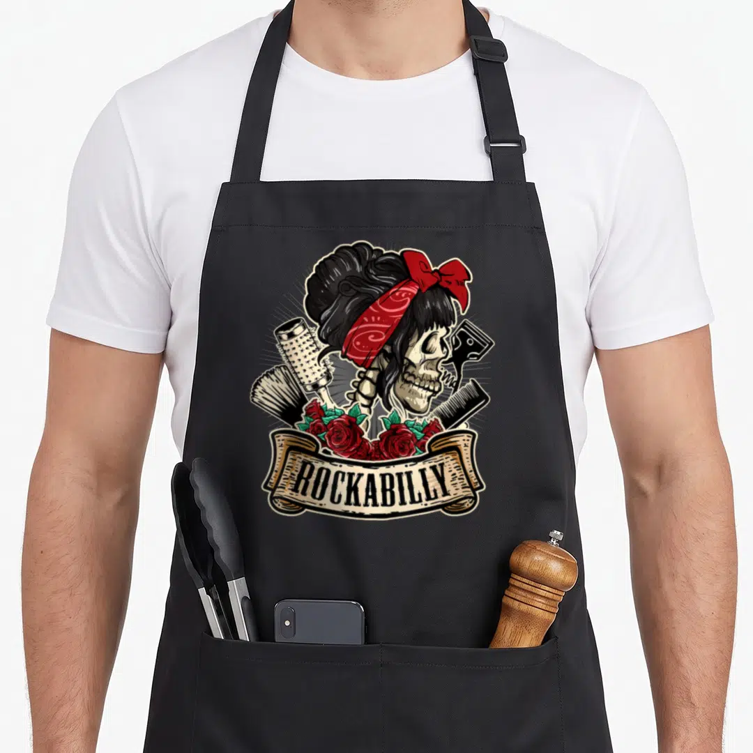 Hairstylist rockabilly apron - Skeleton with red bandana, hairbrush, comb, and roses under beige ROCKABILLY banner — shown on a black cotton canvas apron against a white background