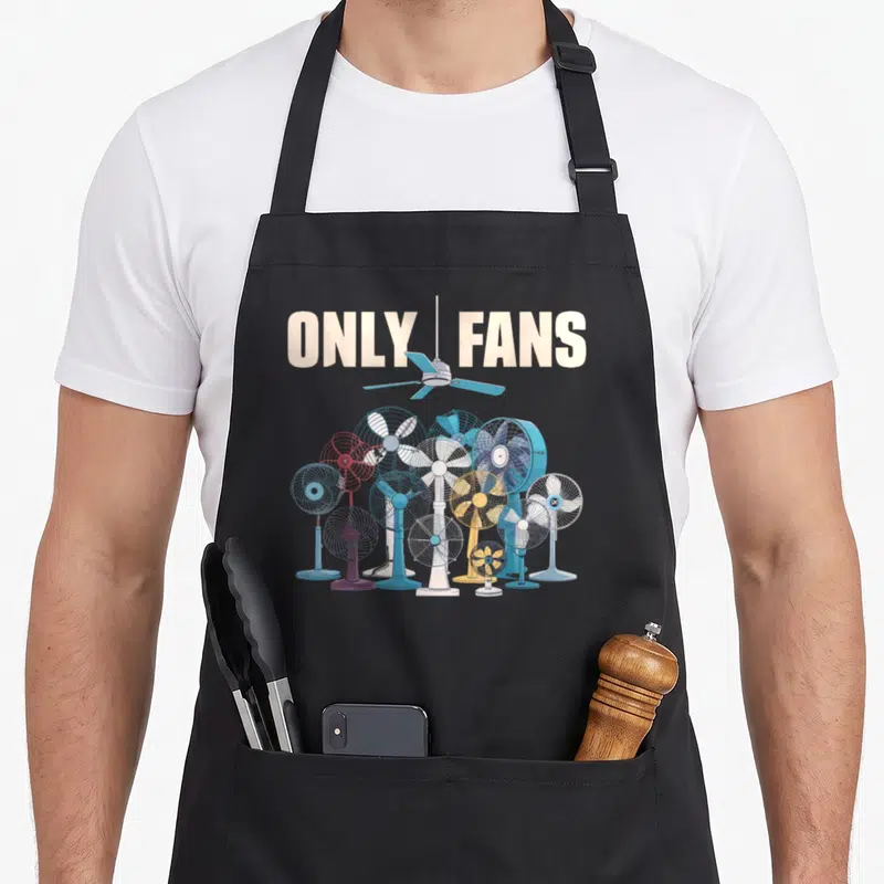 Fan joke apron - ONLY FANS text split by ceiling fan above cluster of electric fans in blue and white cartoon style — shown on a black cotton canvas apron against a white background