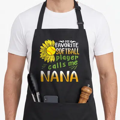 Softball sunflower apron - Sunflower with yellow softball center and stacked text MY FAVORITE SOFTBALL player calls me — shown on a black cotton canvas apron against a white background