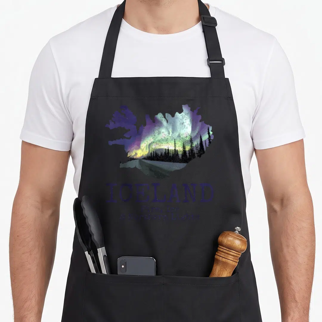 Map icelandic apron - Retro map of Iceland silhouette filled with green aurora and pine trees above dark purple text — shown on a black cotton canvas apron against a white background