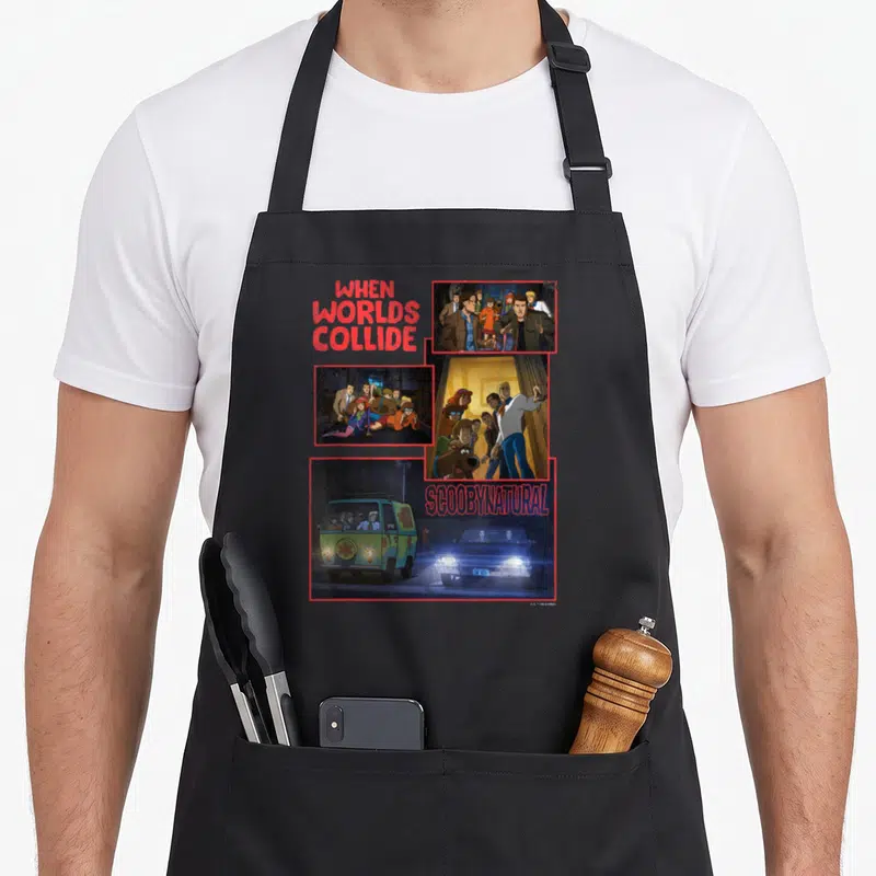 Scoobynitual decade apron - When Worlds Collide Scoobynatural text with three cartoon crossover panels in red blue — shown on a black cotton canvas apron against a white background