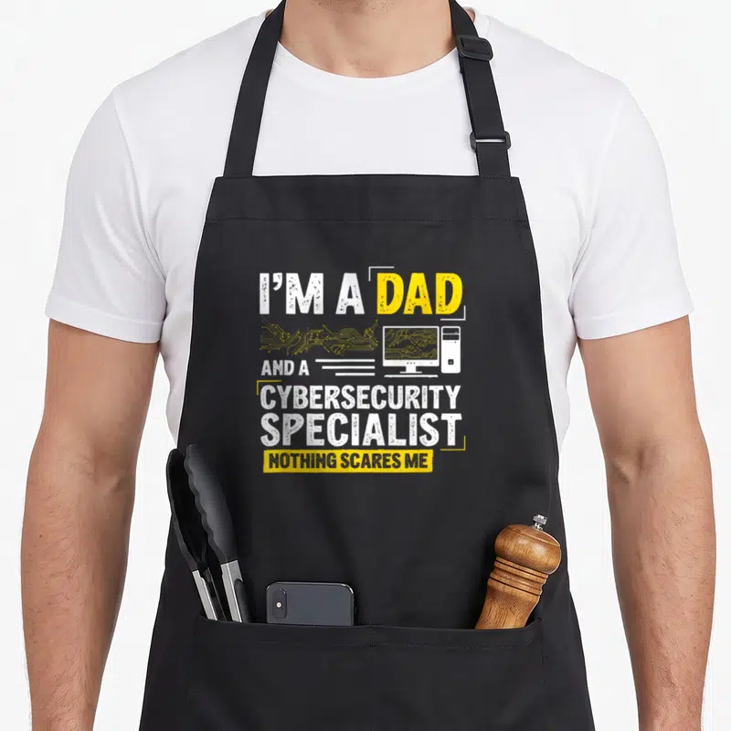 Specialist cybersecurity apron - I'M A DAD AND A CYBERSECURITY SPECIALIST NOTHING SCARES ME text with computer — shown on a black cotton canvas apron against a white background