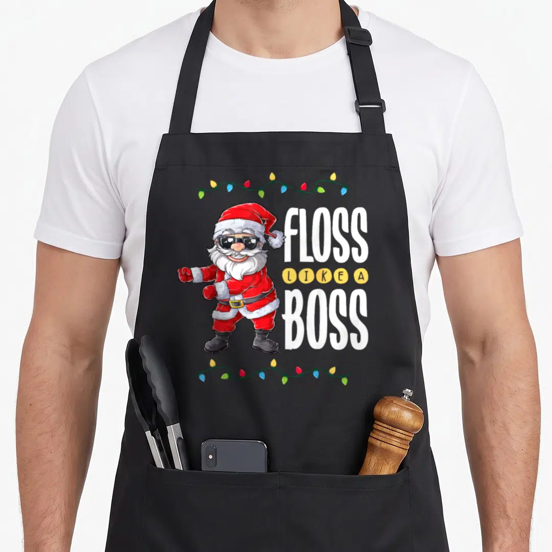 Santa boss apron - Cartoon Santa flossing with sunglasses next to stacked text FLOSS LIKE A BOSS framed by Christmas — shown on a black cotton canvas apron against a white background