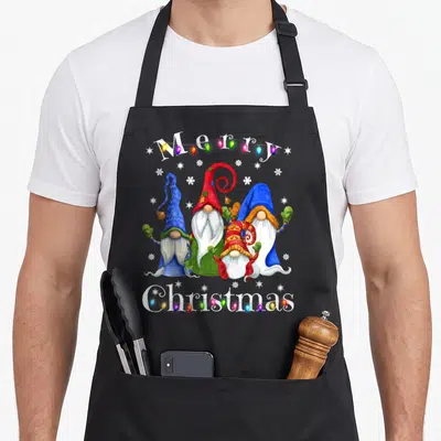 Pajamas merry christmas apron - Four gnomes and multicolored lights with Merry Christmas text in watercolor style — shown on a black cotton canvas apron against a white background