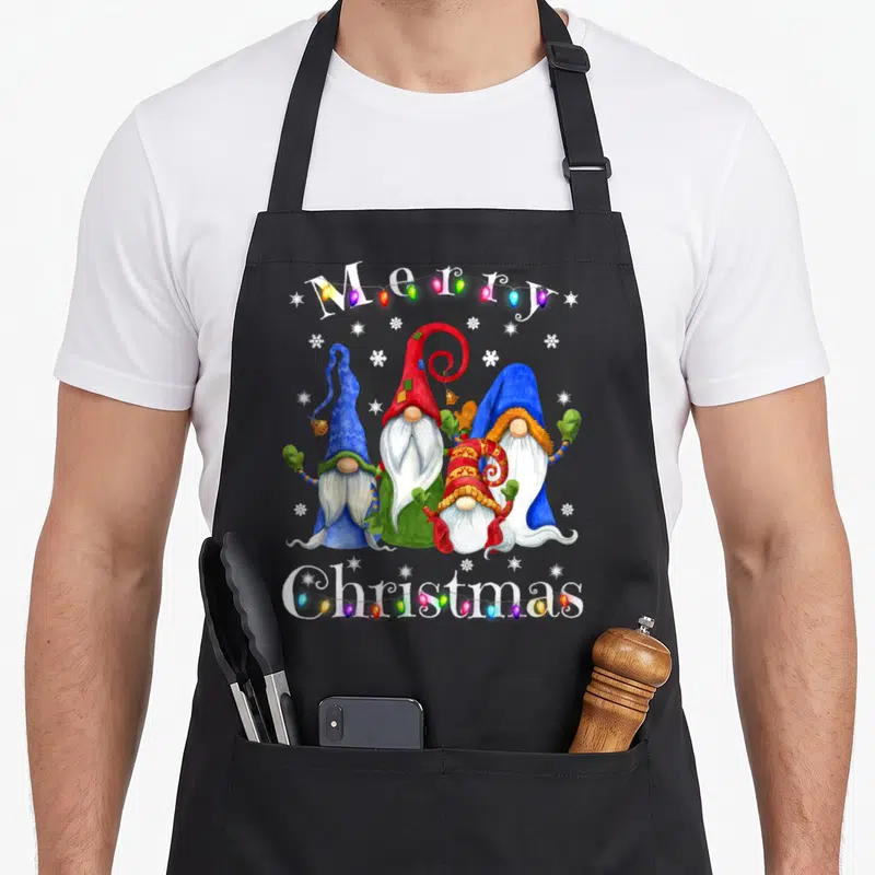Pajamas merry christmas apron - Four gnomes and multicolored lights with Merry Christmas text in watercolor style — shown on a black cotton canvas apron against a white background
