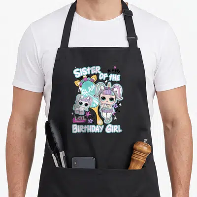 Surprise birthday apron - Sister of the Glam Birthday Girl doll unicorn mirror cartoon print — shown on a black cotton canvas apron against a white background