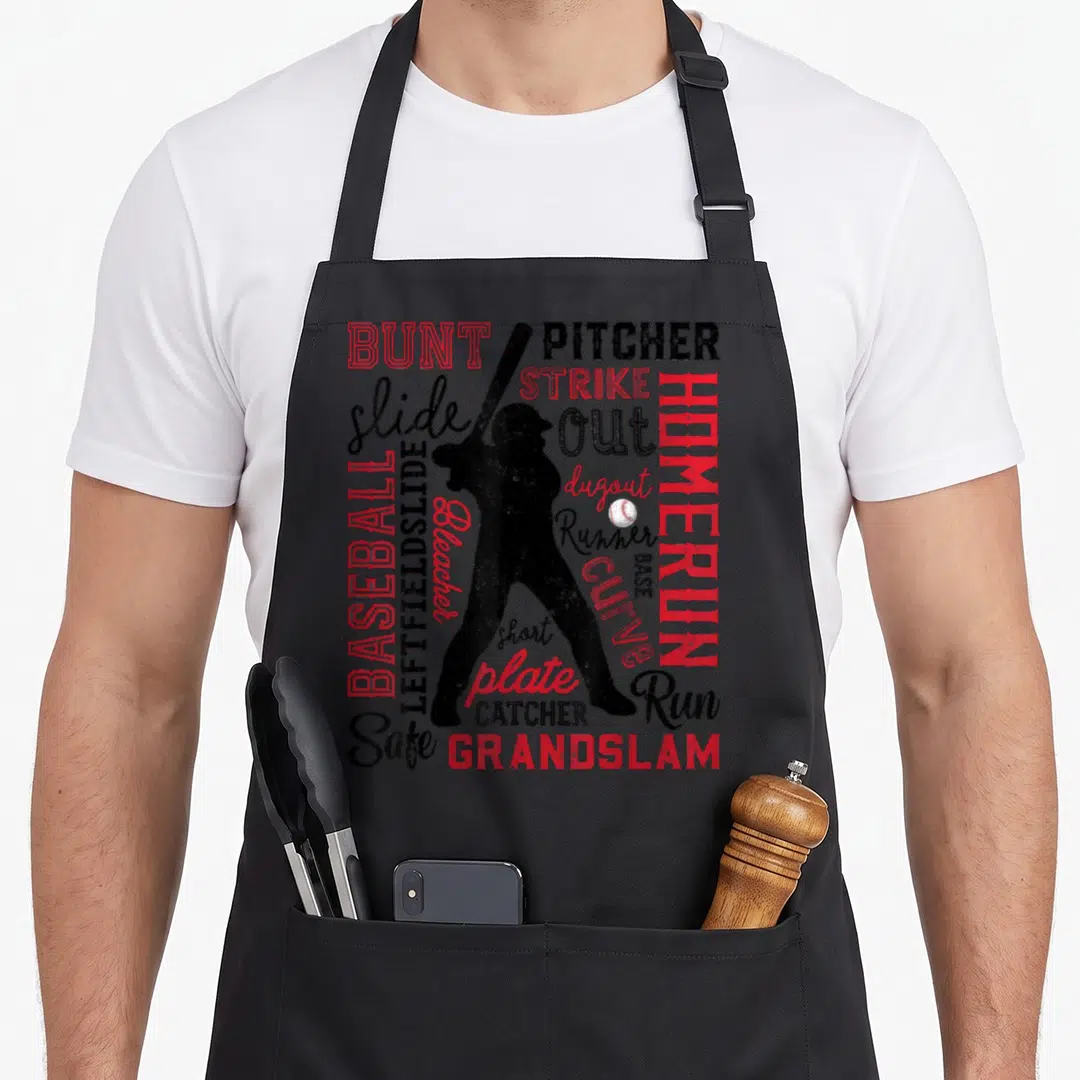Typography baseball apron - Black batter silhouette surrounded by red and black words like BUNT, PITCHER, and HOMERUN — shown on a black cotton canvas apron against a white background