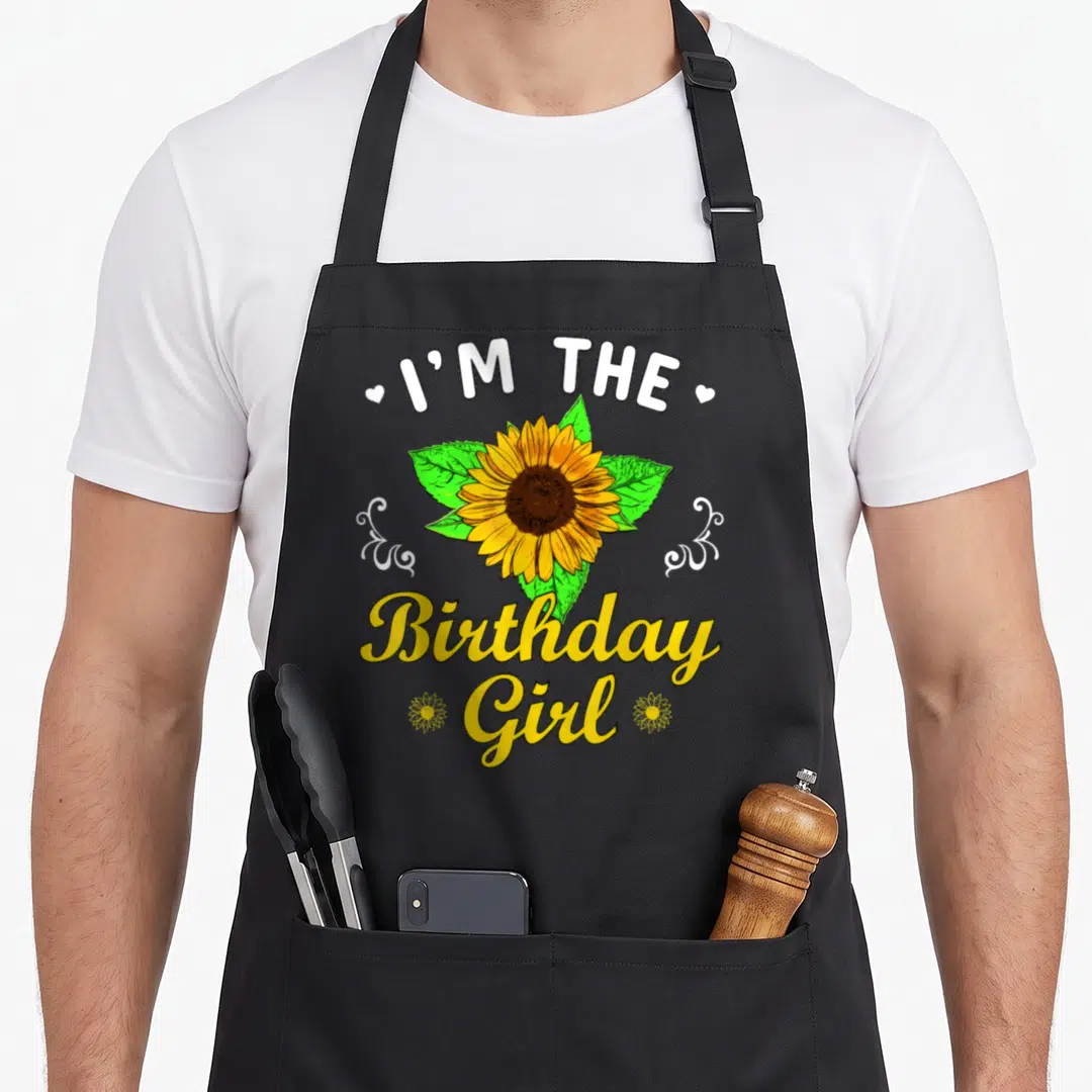 Theme sunflower apron - I'M THE Birthday Girl text with yellow sunflower and white swirls — shown on a black cotton canvas apron against a white background
