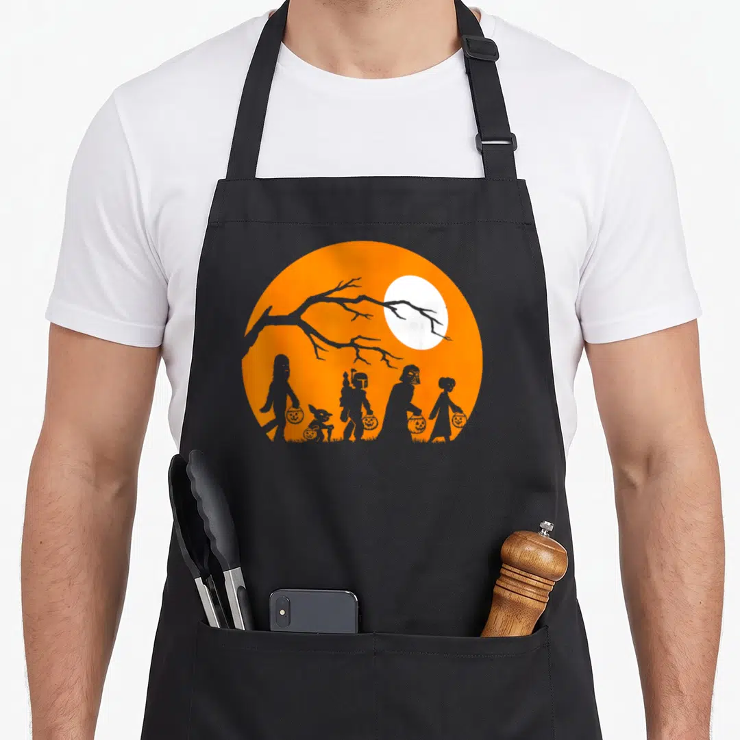 Trick halloween apron - Grey silhouettes holding pumpkin buckets inside an orange circle with a white moon and tree — shown on a black cotton canvas apron against a white background