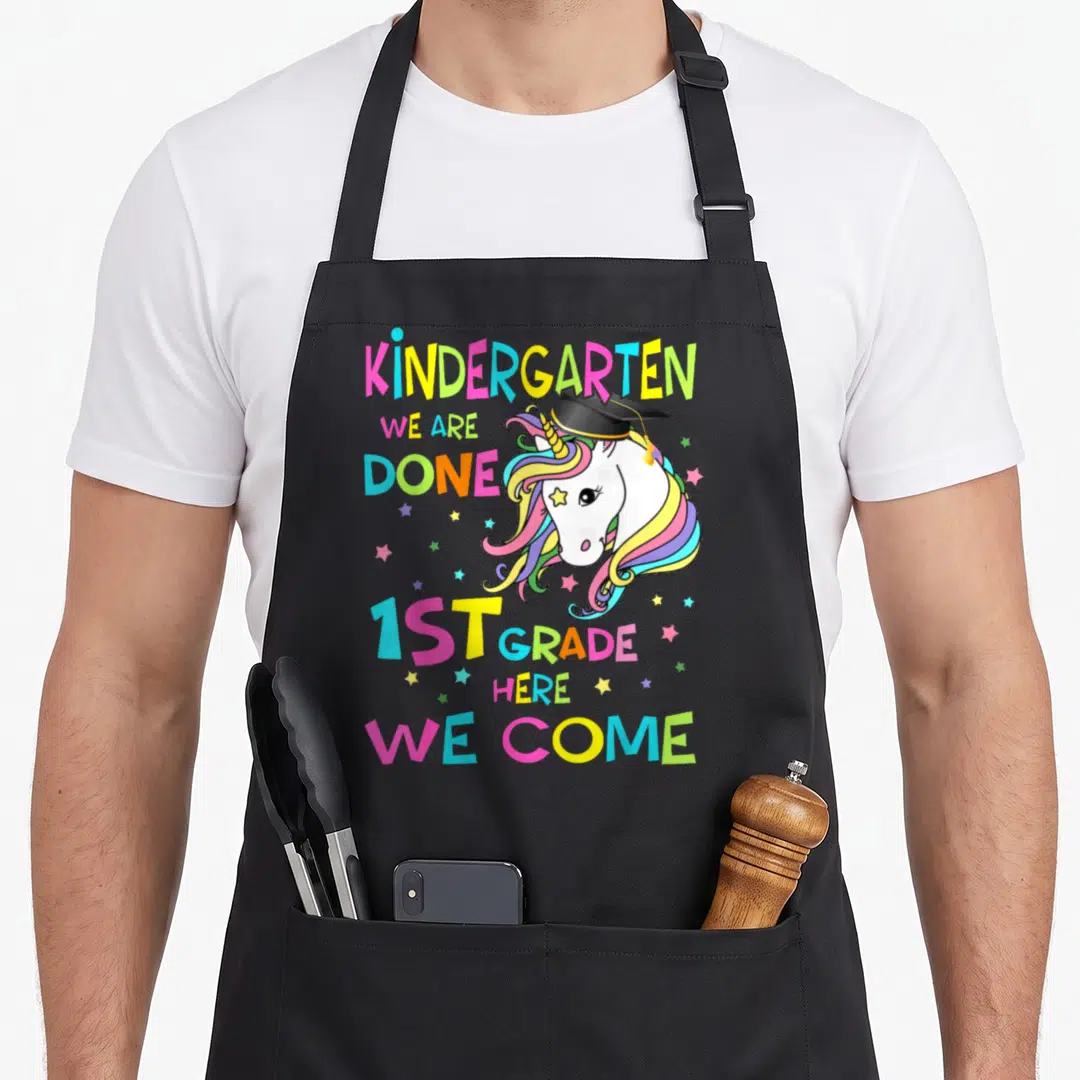 Kindergarten graduation magical unicorn aprons - Cartoon unicorn head in graduation cap with rainbow mane and colorful — shown on a black cotton canvas apron against a white background