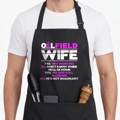Roughneck wife apron - Pink and white OILFIELD WIFE text with oil rig inside O and stacked yes no answers — shown on a black cotton canvas apron against a white background