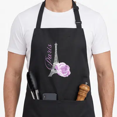 Souvenir paris apron - White Eiffel Tower with vertical pink Paris text and overlapping pink rose — shown on a black cotton canvas apron against a white background