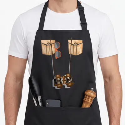 Jungle halloween apron - Cartoon binoculars with zebra stripes, tan pockets, and orange glasses hanging between straps — shown on a black cotton canvas apron against a white background