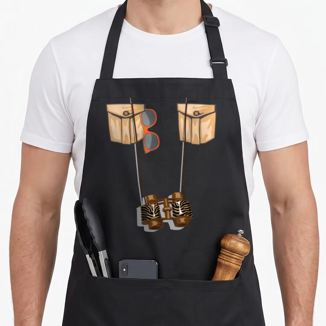 Jungle halloween apron - Cartoon binoculars with zebra stripes, tan pockets, and orange glasses hanging between straps — shown on a black cotton canvas apron against a white background