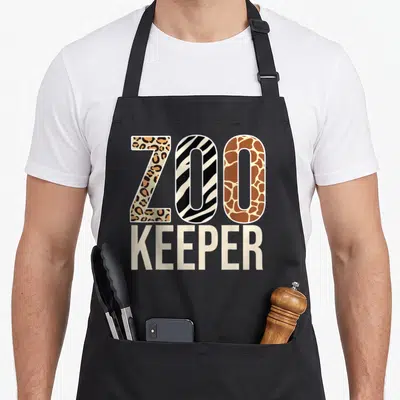 Zookeeper animal apron - ZOO KEEPER text with leopard, zebra, and giraffe pattern fills in brown black and beige — shown on a black cotton canvas apron against a white background
