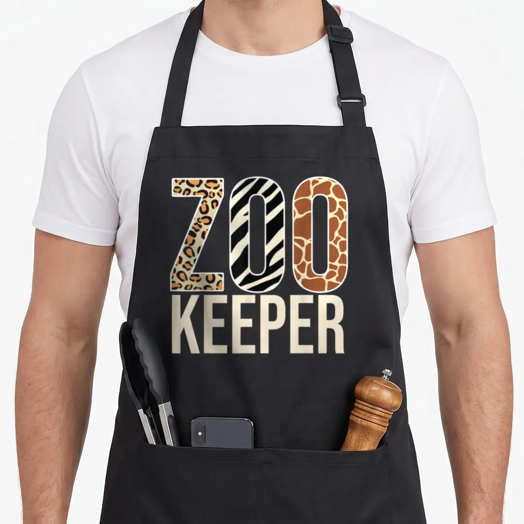 Zookeeper animal apron - ZOO KEEPER text with leopard, zebra, and giraffe pattern fills in brown black and beige — shown on a black cotton canvas apron against a white background